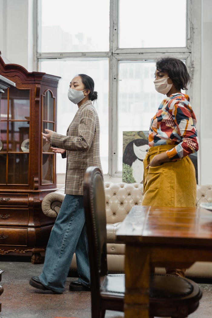 gallery-5 Two women wearing masks shop for antiques in a stylish store setting.