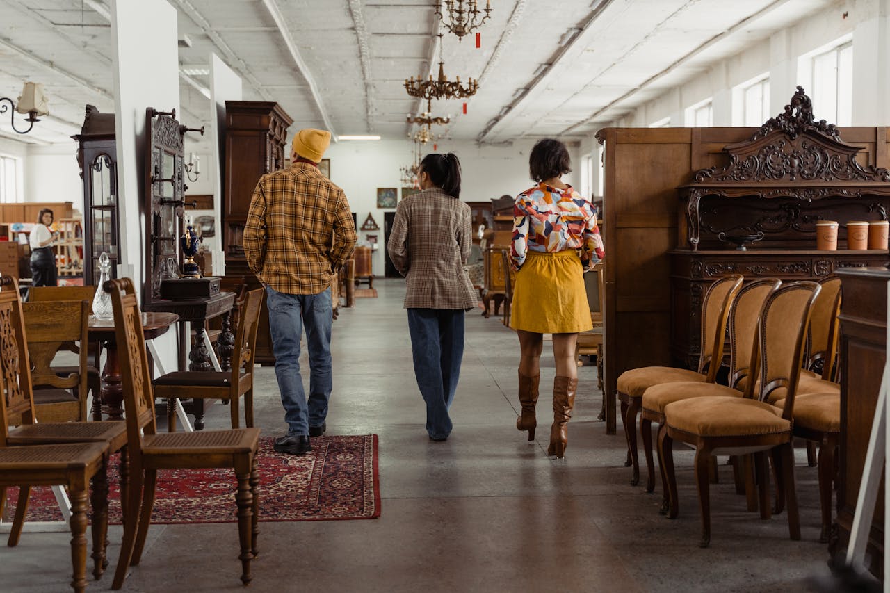 hero-img-01 People walking through an antique furniture store, surrounded by vintage chairs and decor.