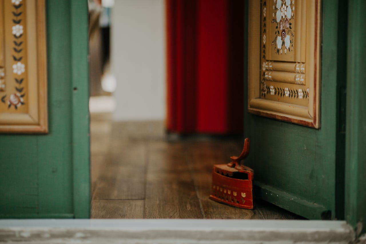 why-choose-us A decorative green door slightly ajar with an antique iron on wooden flooring.
